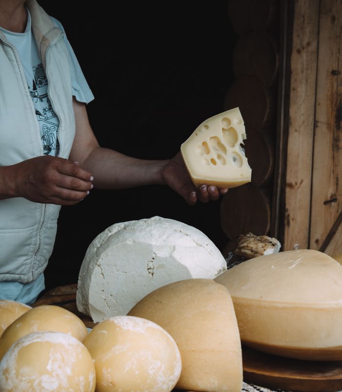 Close-up of various cheeses displayed on a rustic wooden table with a person holding a slice.